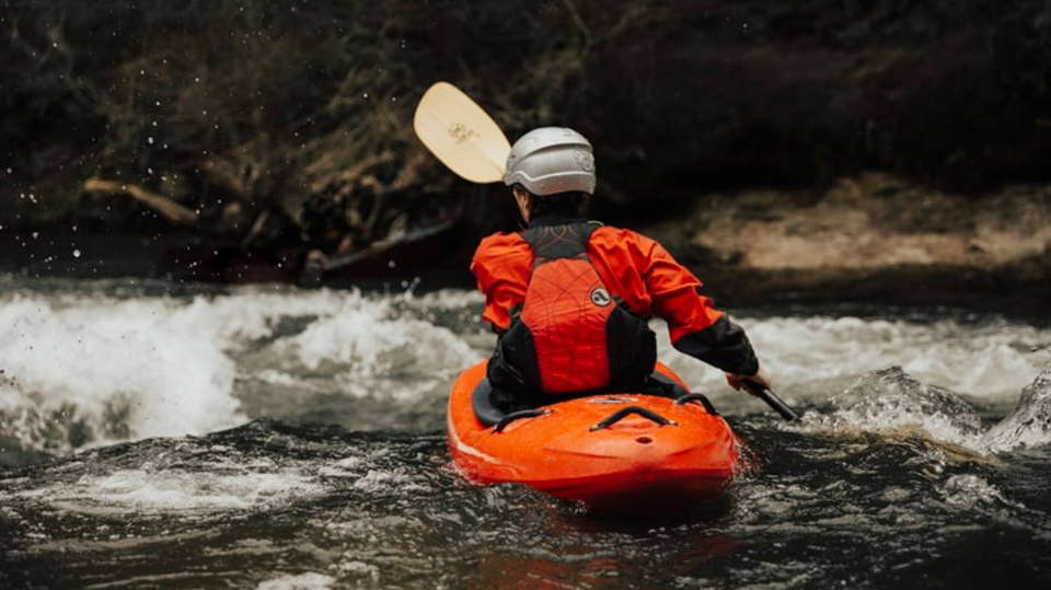 Man in red water rafting gear on orange kayak going over rapids