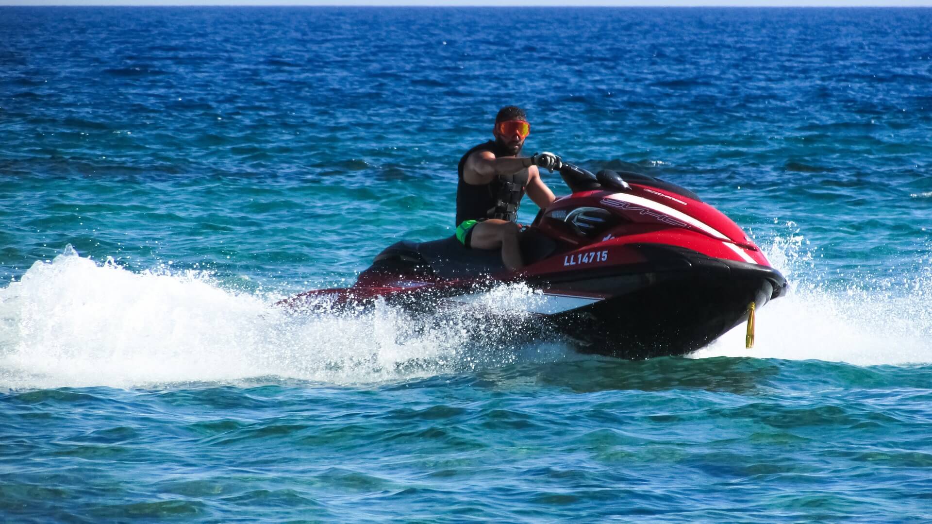 Man riding red jetski going fast over waves on blue sea