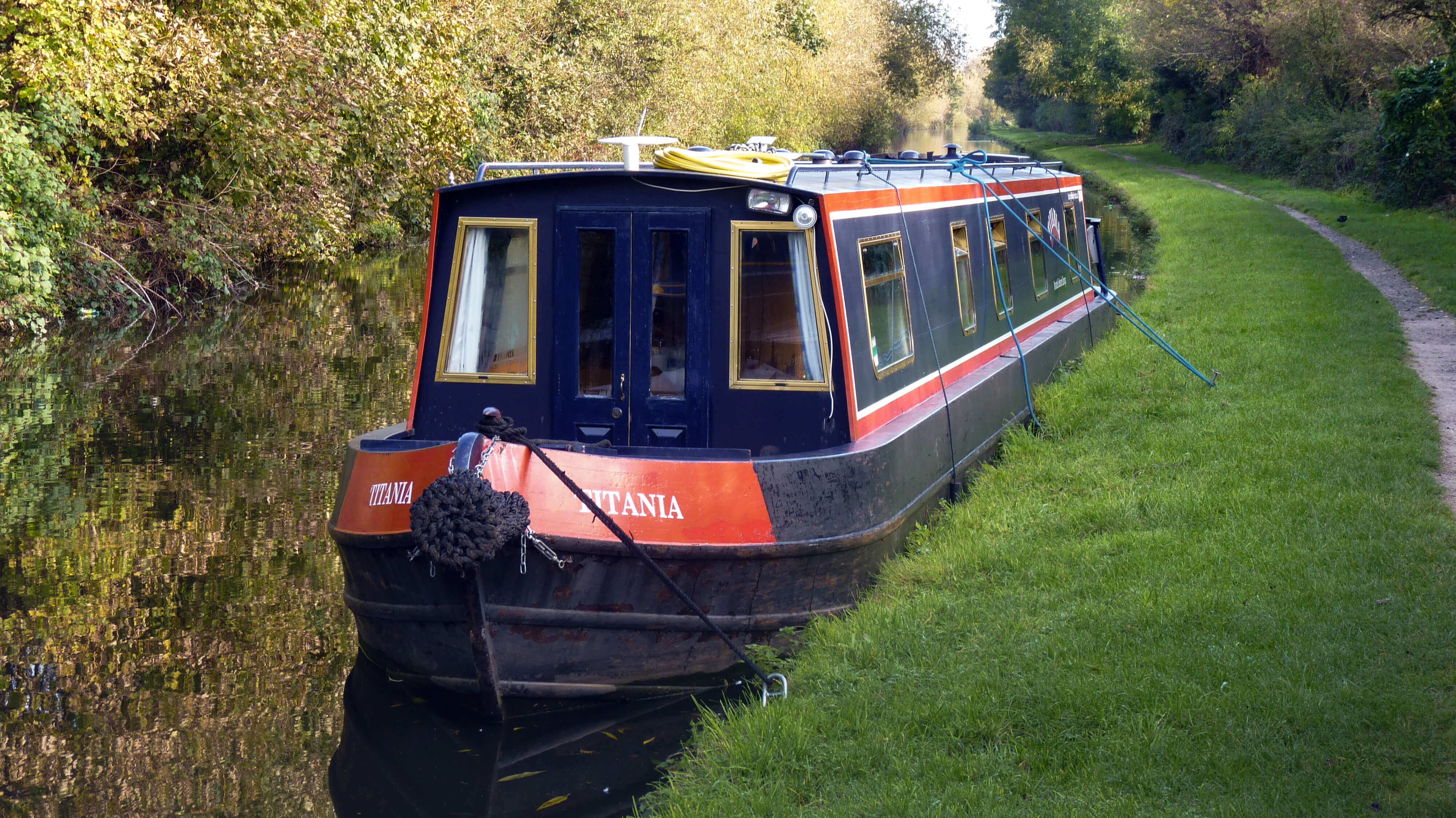 Navy blue and red narrowboat moored on the side of canal