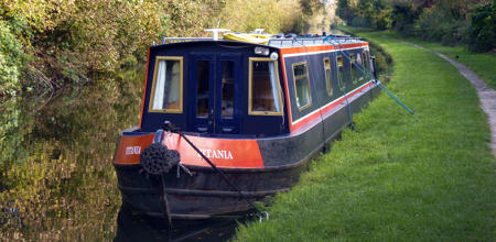 Navy blue and red narrowboat moored on the side of canal