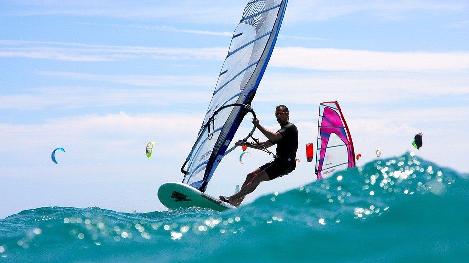 Man using windsurfer on clear blue sea with kites behind him